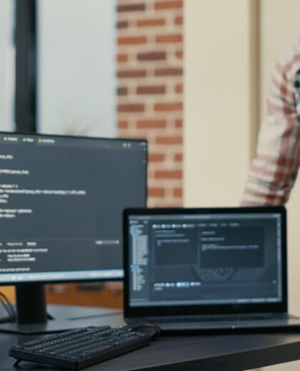 focused-software-developer-writing-code-laptop-looking-multiple-screens-with-programming-language-is-interrupted-by-colleague-coder-asking-advice-programmers-doing-online-cloud-computing (1)